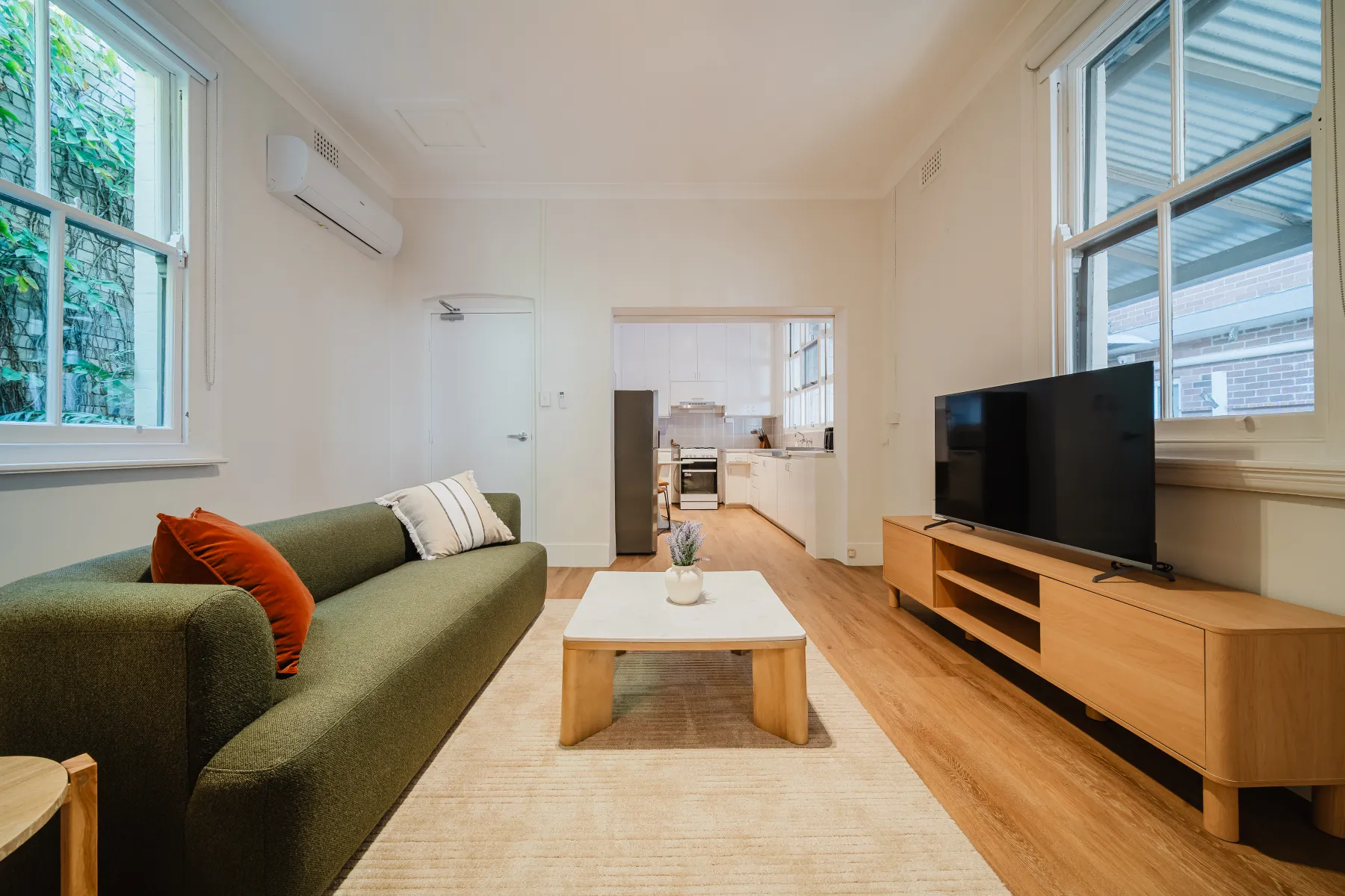 Bright open-plan living room with a green sofa and kitchen beyond at Sareh Balmain