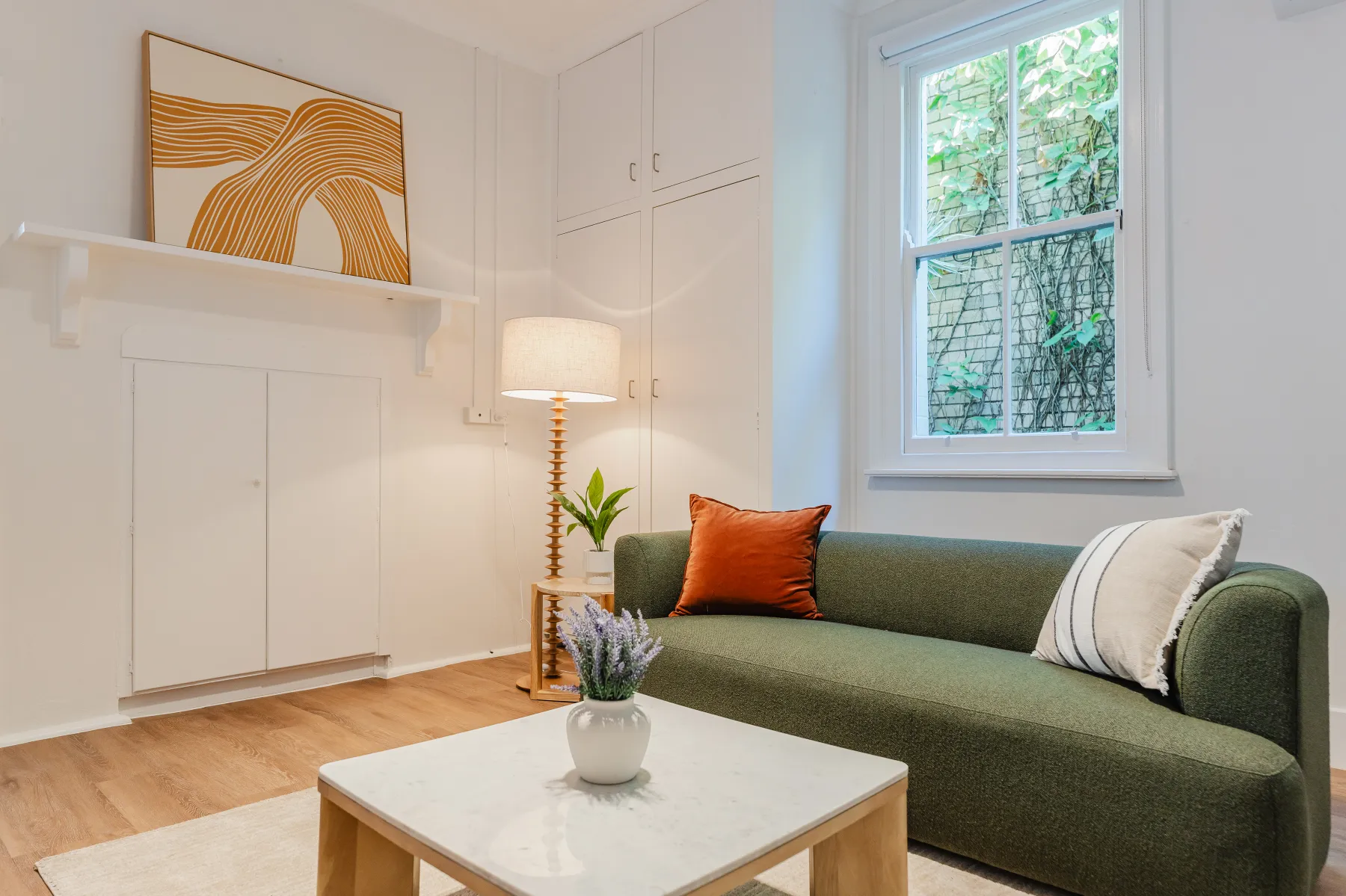 A cosy lounge with a green sofa, warm lamp and leafy outlook